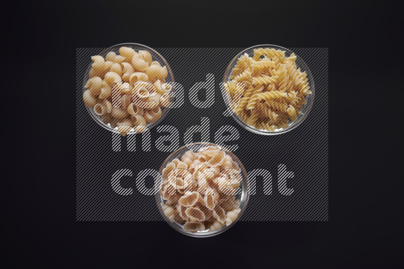 Different pasta types in glass bowls on black background