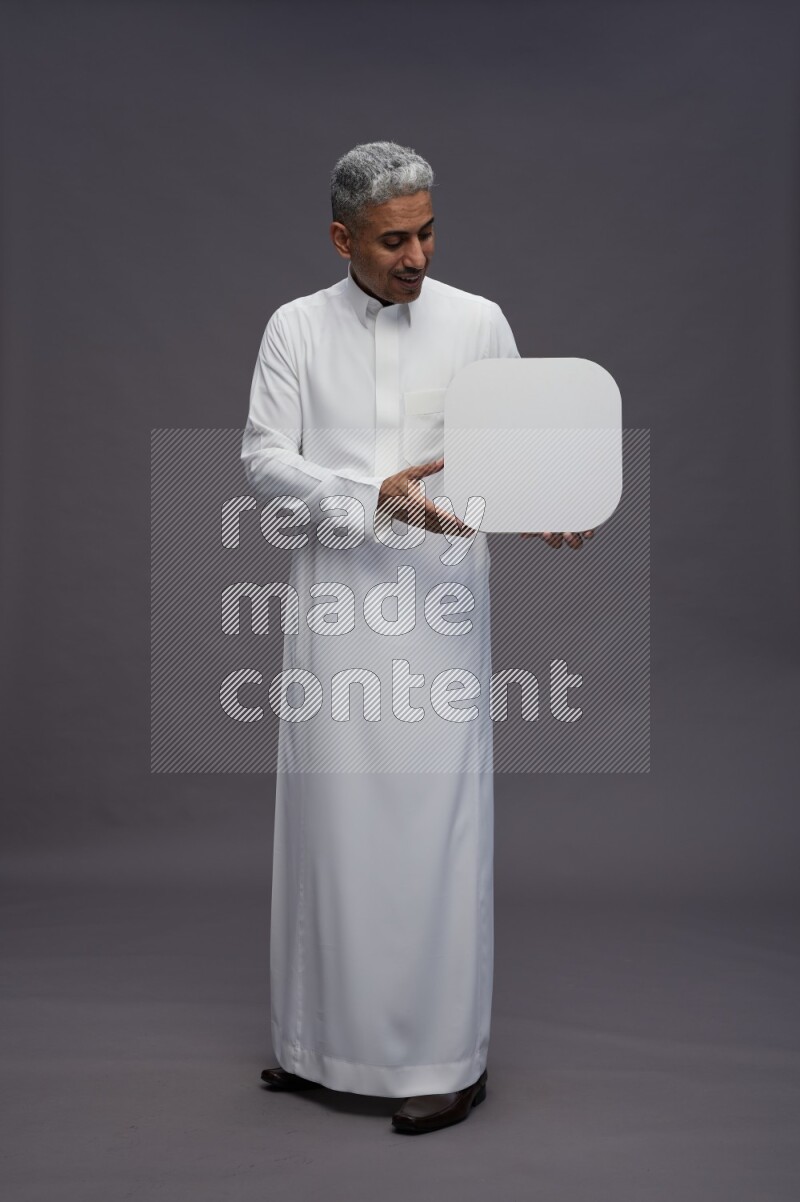 Saudi man wearing thob standing holding social media sign on gray background