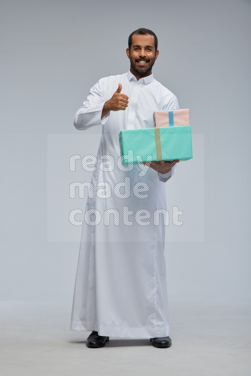 Saudi man Wearing thob standing holding gift box on Gray background