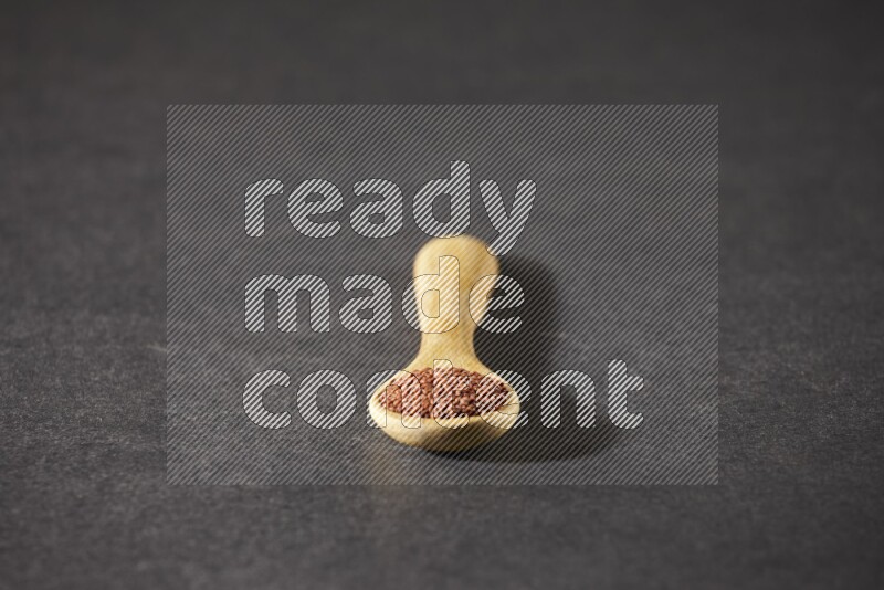 A wooden spoon full of garden cress seeds on a black flooring