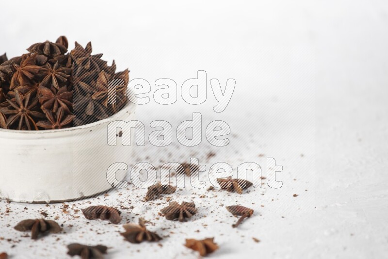 Star Anise in a white bowl and more of it sprinkled on white background