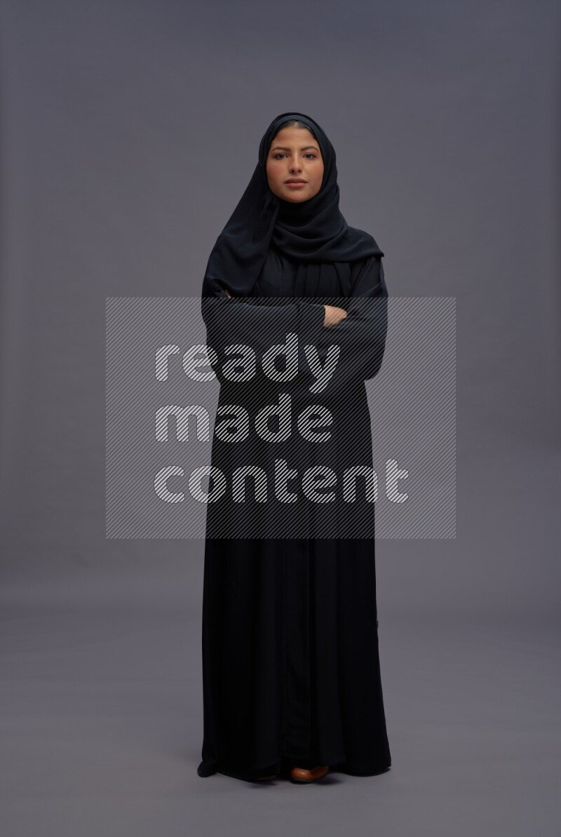 Saudi woman wearing Abaya standing with crossed arms on gray background