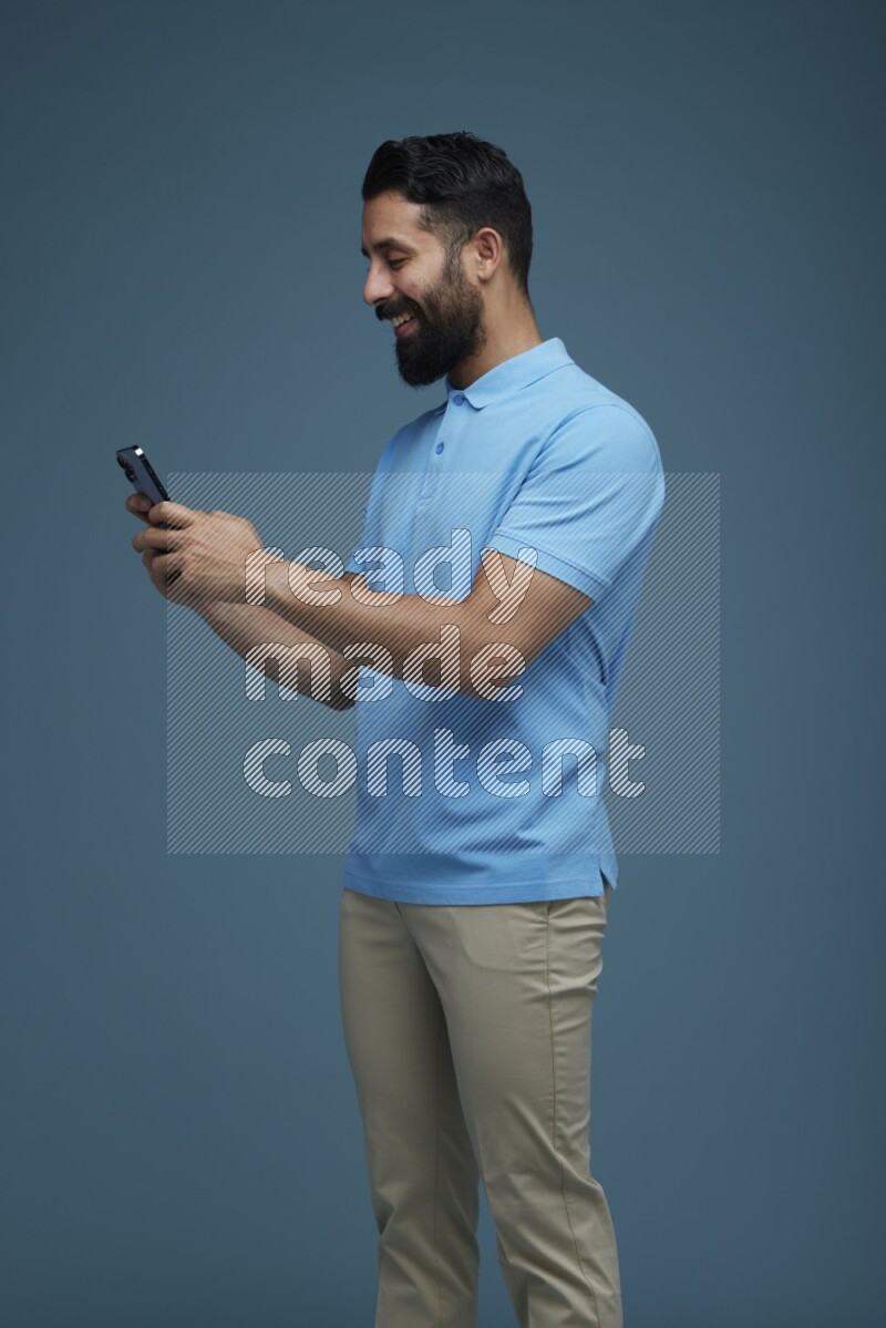 A man Texting on his phone in a blue background wearing a Blue shirt