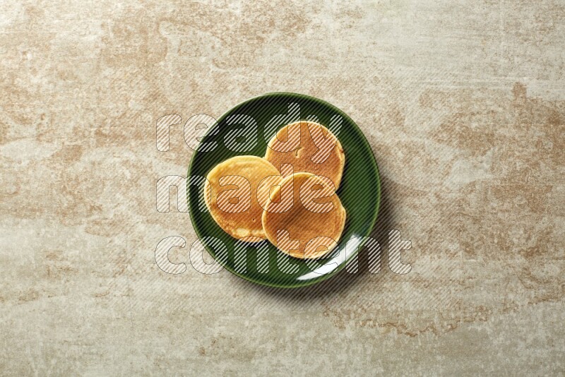 Three stacked plain mini pancakes in a green plate on beige background