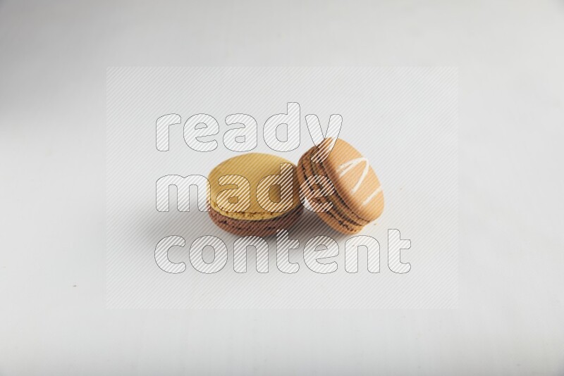 45º Shot of of two assorted Brown Irish Cream, and Yellow, and Brown Chai Latte macarons on white background