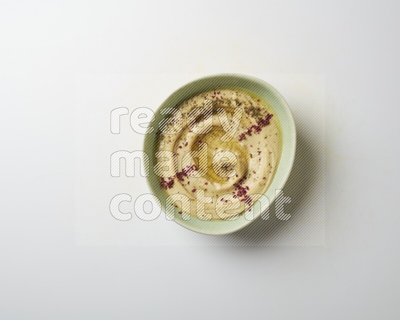 Hummus in a green plate garnished with zattar & sumak on a white background