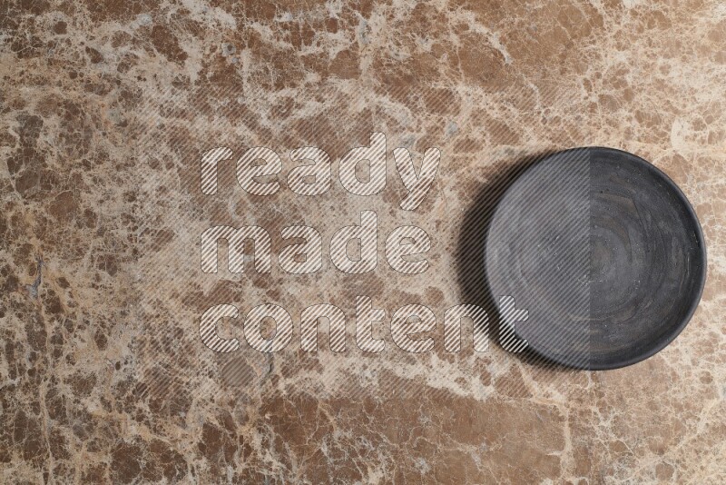 A circular black pottery plate on beige marble background