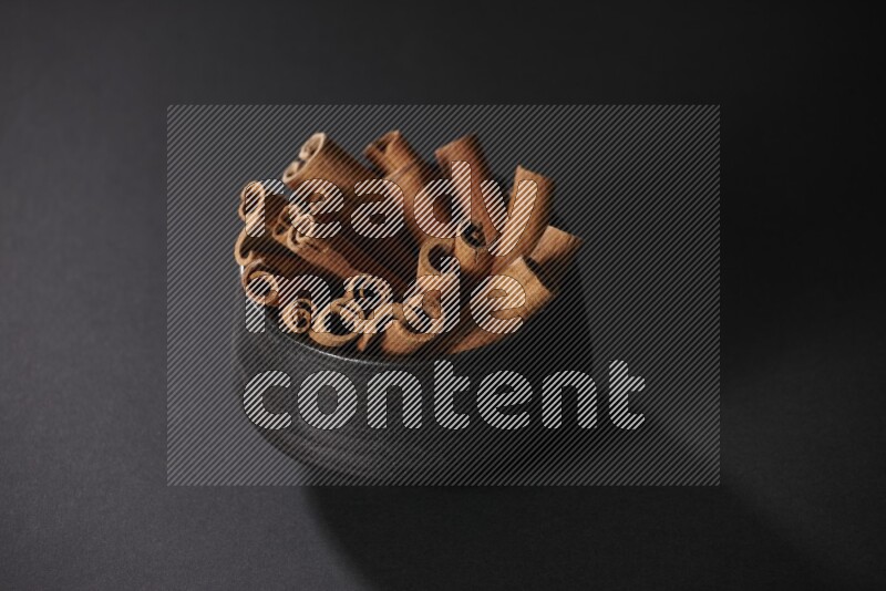 Cinnamon sticks in a black bowl on a black background in different angles