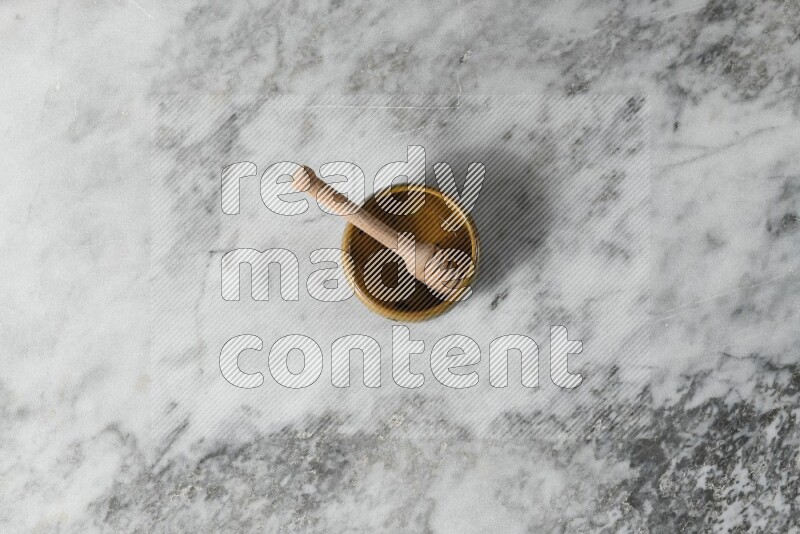 Multicolored pottery bowl with wooden honey dipper in it on grey marble background