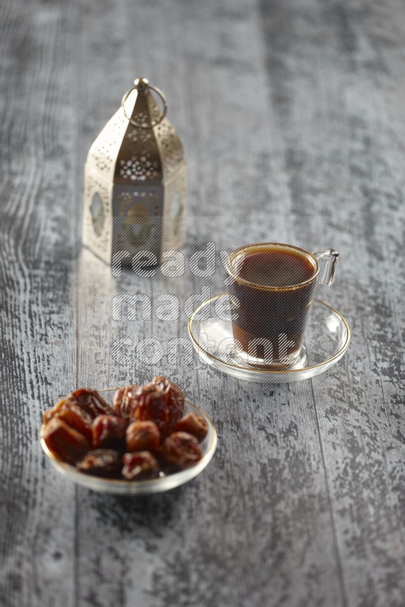 A silver lantern with different drinks, dates, nuts, prayer beads and quran on grey wooden background