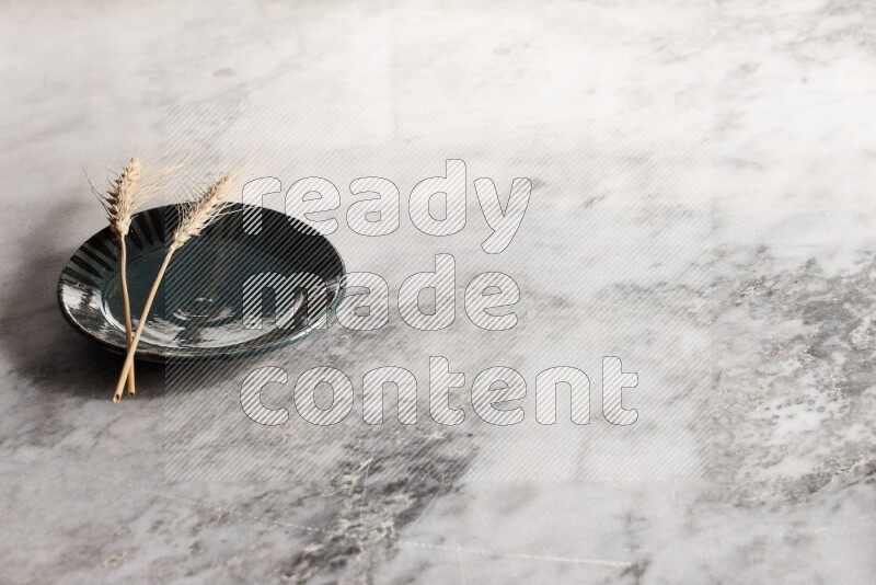 Wheat stalks on multicolored pottery plate on grey marble background