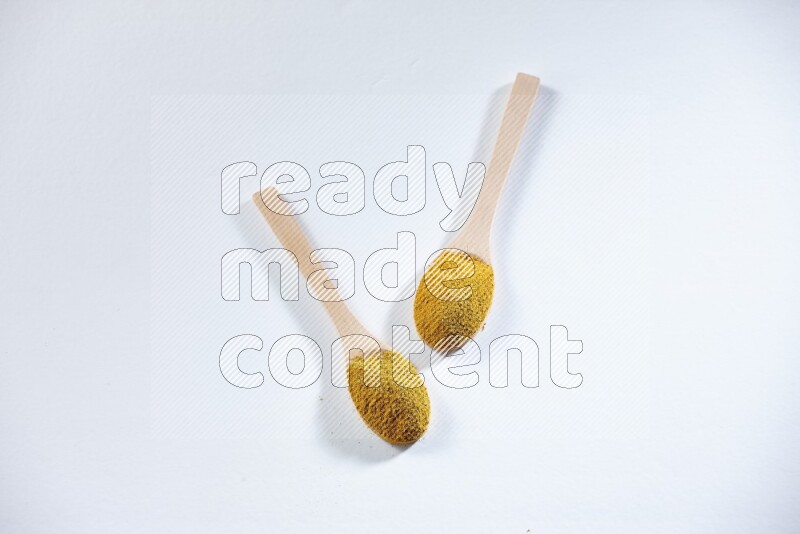 ملعقتان خشبيتان ممتلئتان ببودرة الكركم على خلفية بيضاء