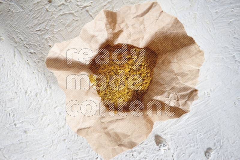 Turmeric powder in a crumpled piece of paper on textured white flooring