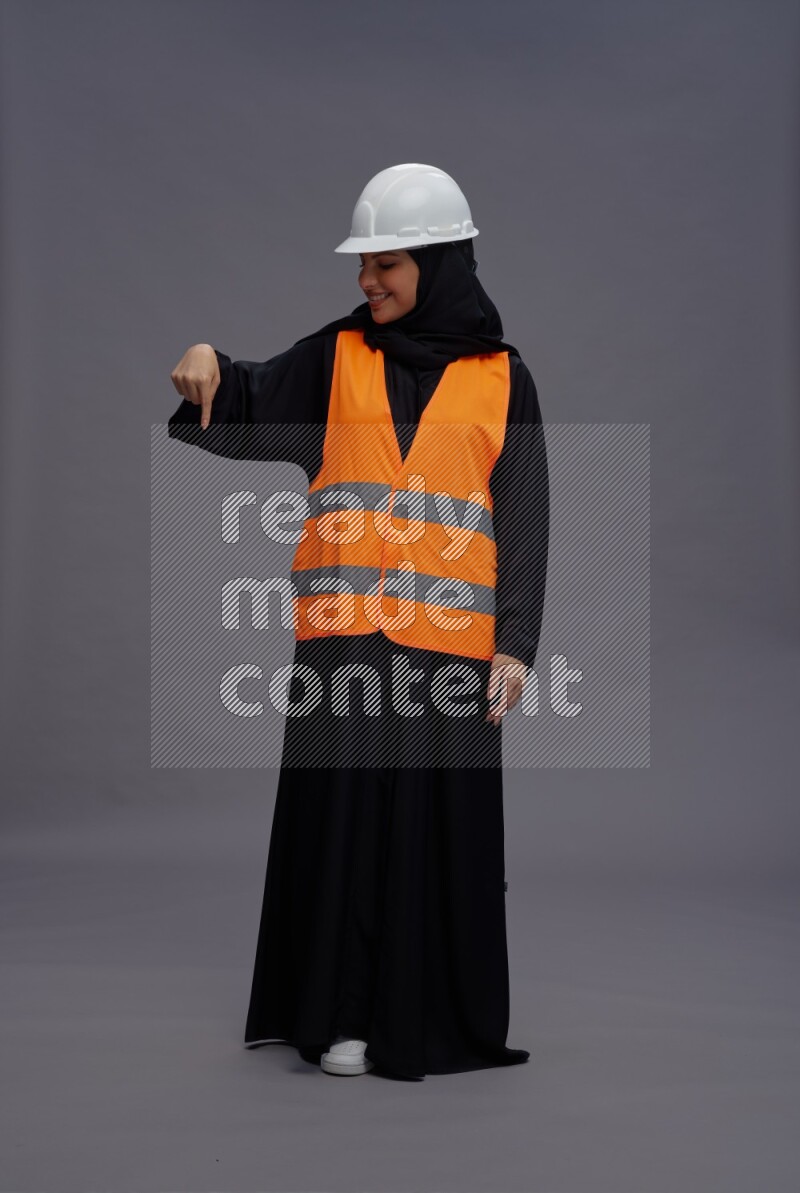 Saudi woman wearing Abaya with engineer vest standing interacting with the camera on gray background