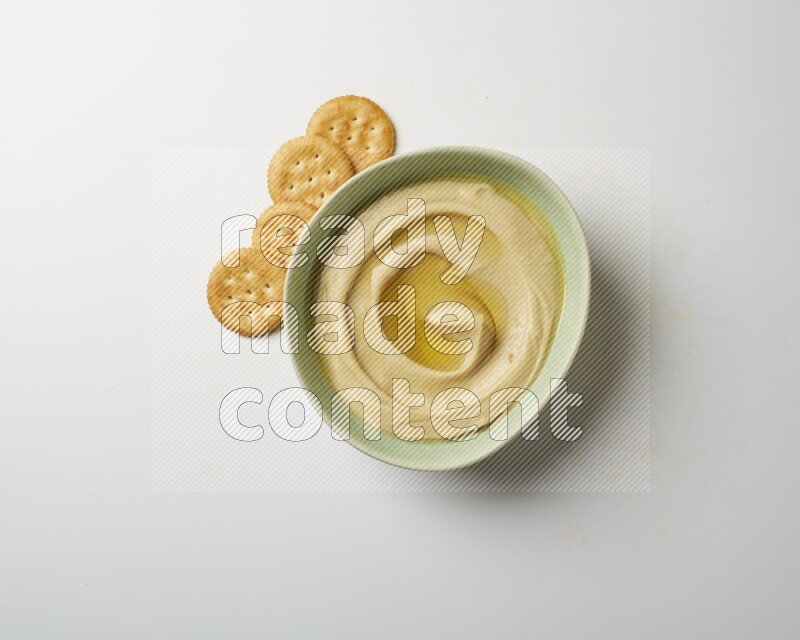 Hummus in a green plate garnished with olive oil on a white background