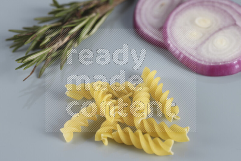 Raw pasta with different ingredients such as cherry tomatoes, garlic, onions, red chilis, black pepper, white pepper, bay laurel leaves, rosemary, cardamom and mushrooms on light blue background