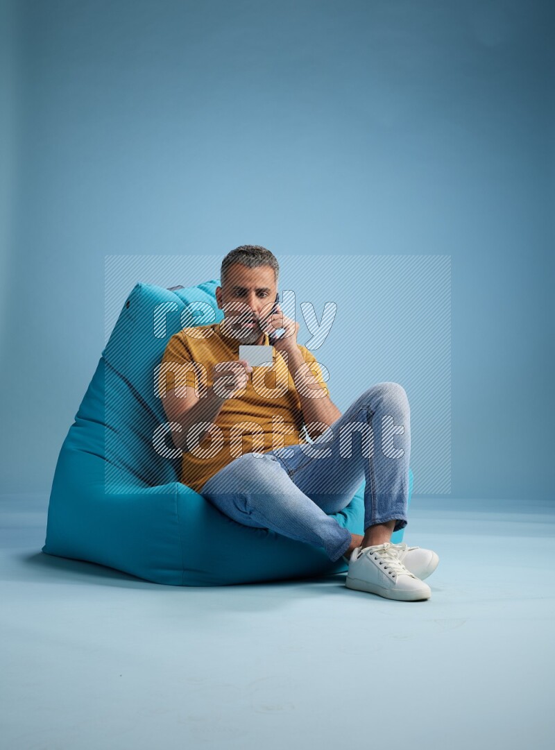 A man sitting on a blue beanbag and holding ATM card with phone