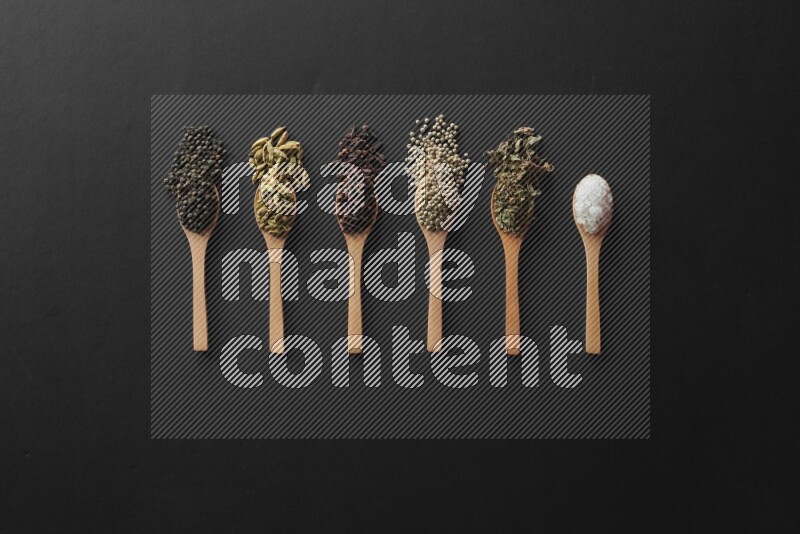 wooden spoons filled with white peppers, cloves, cardamom, salt, black peppers and basil on black flooring