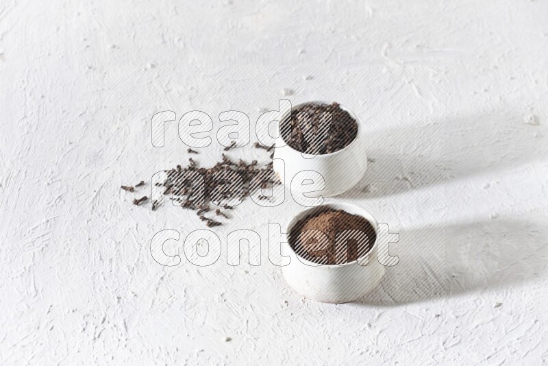 2 Beige ceramic bowls, one full of cloves and the other full of powder on textured white flooring
