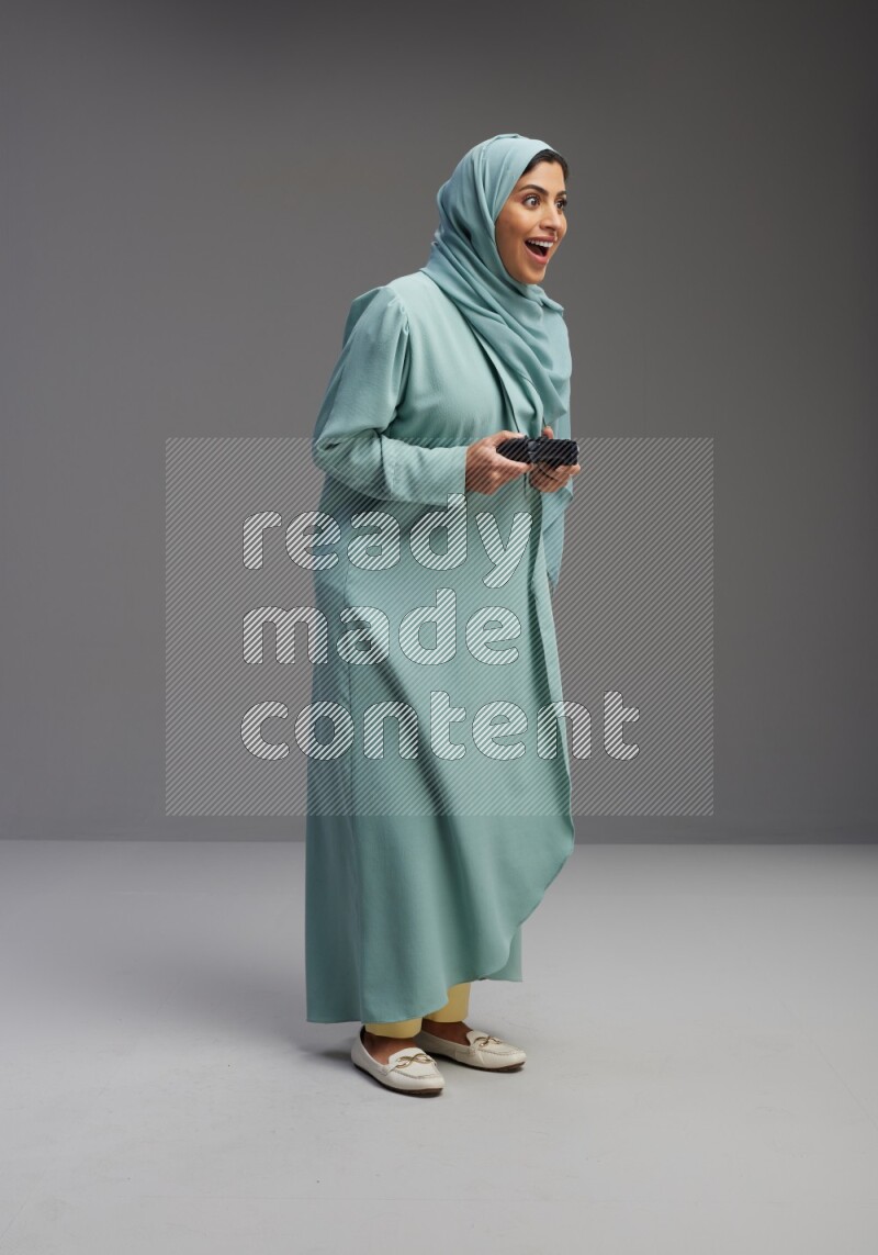 Saudi Woman wearing Abaya standing Playing Games on Gray background