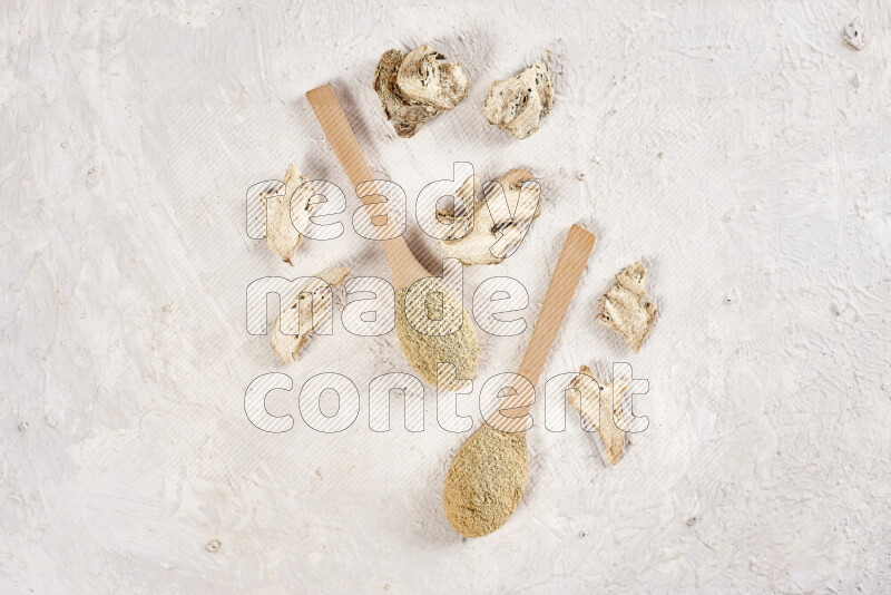 Two wooden spoons full of ground ginger powder on white background