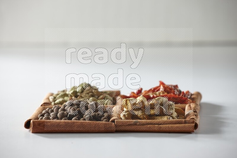 4 مربعات من أعواد القرفة ممتلئة بالفلفل الأحمر المجفف والهيل وأصابع الكركم وبهار الفلفل الحلو على أرضية بيضاء