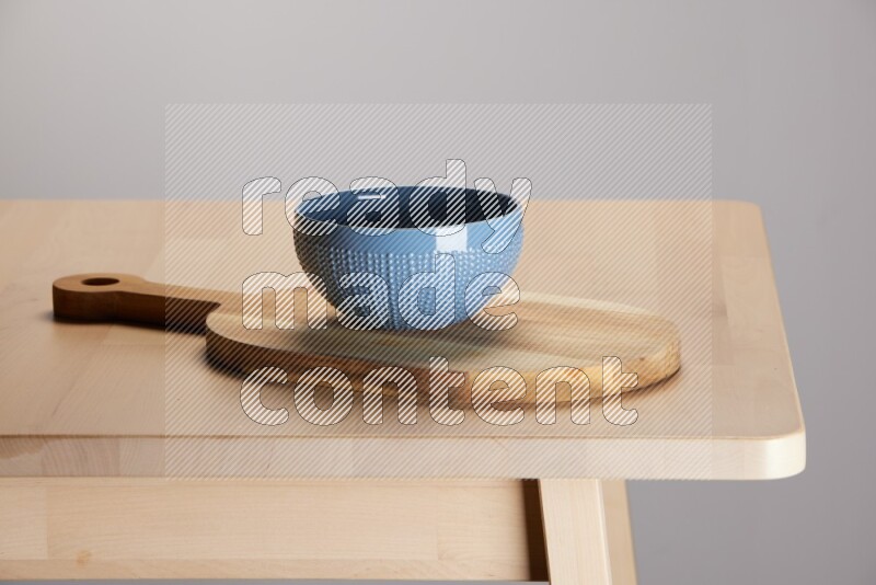 blue bowl placed on a  wooden oval cutting board on the edge of wooden table