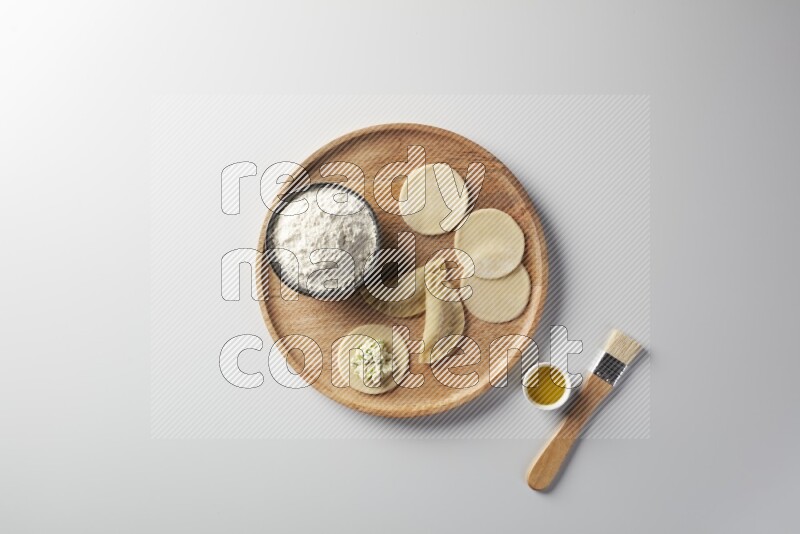 two closed sambosas and one open sambosa filled with cheese while flour, and oil with oil brush aside in a wooden dish on a white background