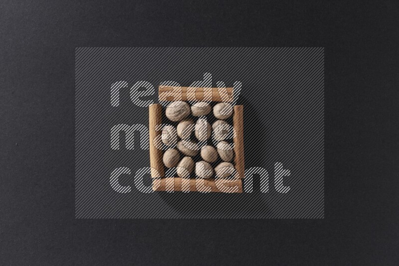 أربعة من أعواد القرفة مكونة شكل مربع بداخلها جوزة الطيب علي خلفية سوداء