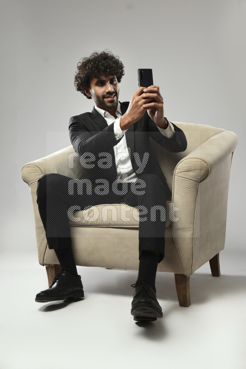 A man wearing formal sitting on a chair shooting with his phone on white background