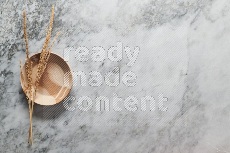 Wheat stalks on multicolored pottery plate on grey marble background