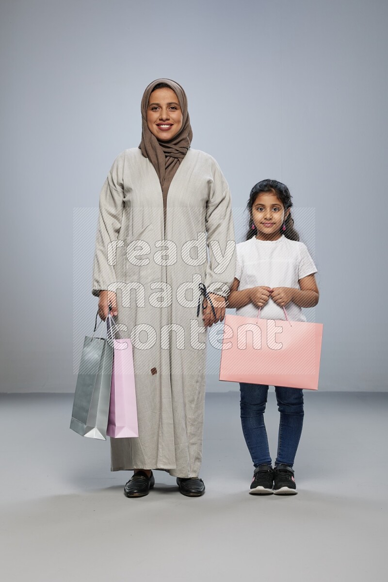 Mom and daughter holding shopping bags on gray background