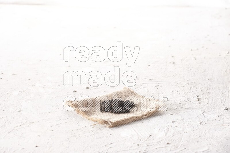 Black pepper on burlap fabric on a textured white flooring