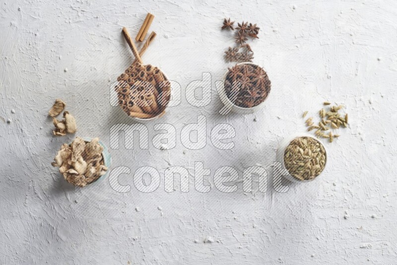 Cardamom, ginger, cinnamon sticks and star anise in 4 bowls on a textured white background