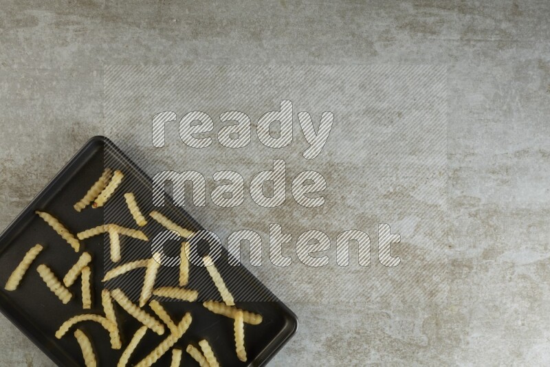 crinkle fries in a black stainless steel rectangle tray on grey textured counter top
