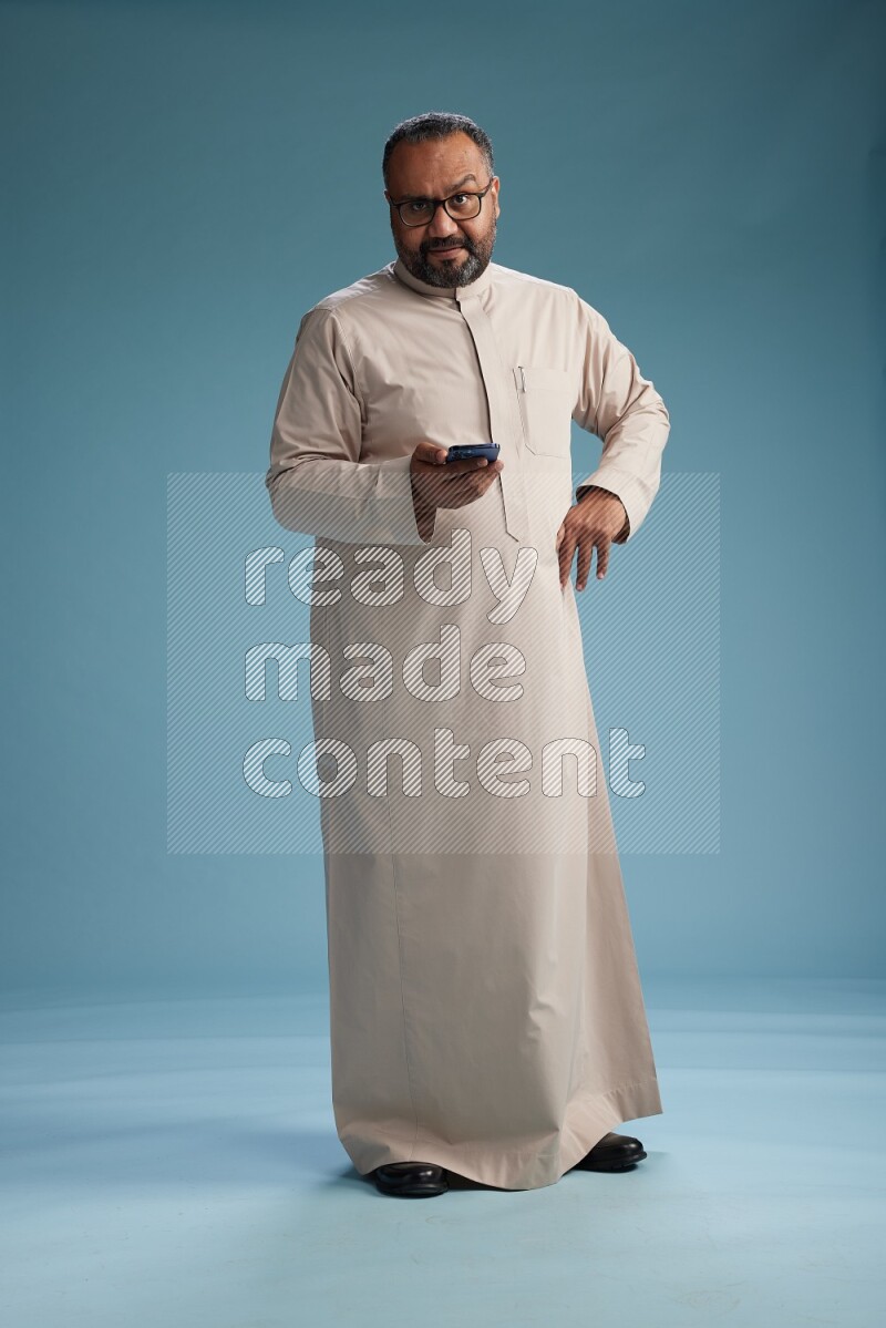 Saudi Man without shimag Standing texting on phone on blue background