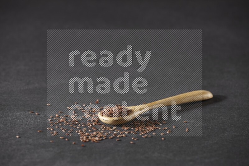 ملعقة خشبية ممتلئة بحبوب بذر الكتان وبعض البذور متناثرة علي خلفية سوداء