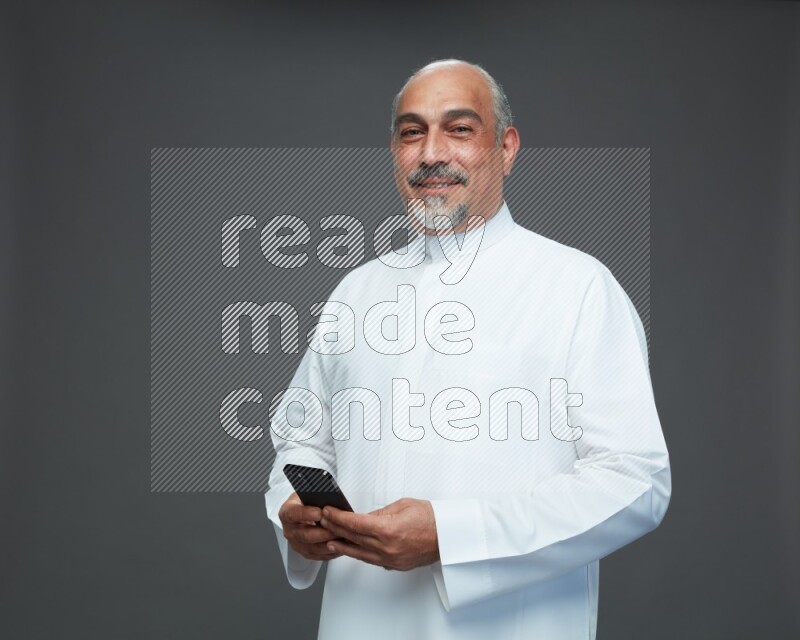 Saudi man without shomag Standing texting on phone on gray background