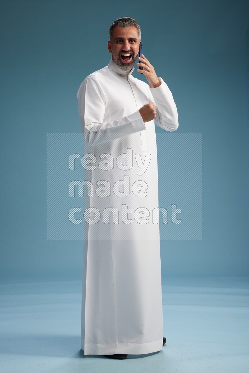 Saudi man wearing thob talking on the phone on blue background