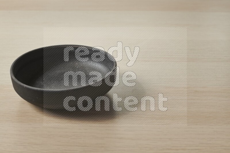 A black pottery bowl on light wooden background