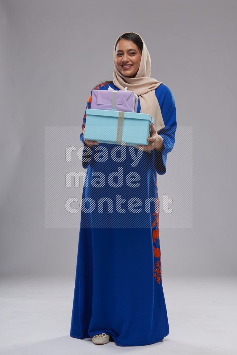 A Saudi woman standing wearing Jalabeya holding a gift box