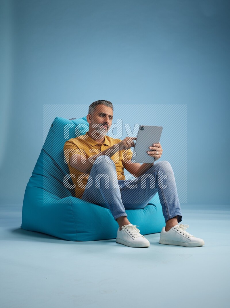 A man sitting on a blue beanbag and working on tablet
