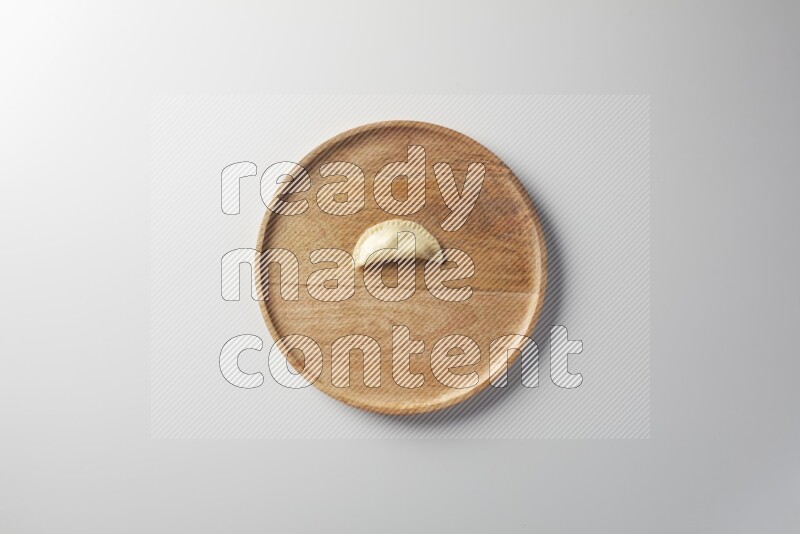 A single Sambosa on a wooden round plate on a white background