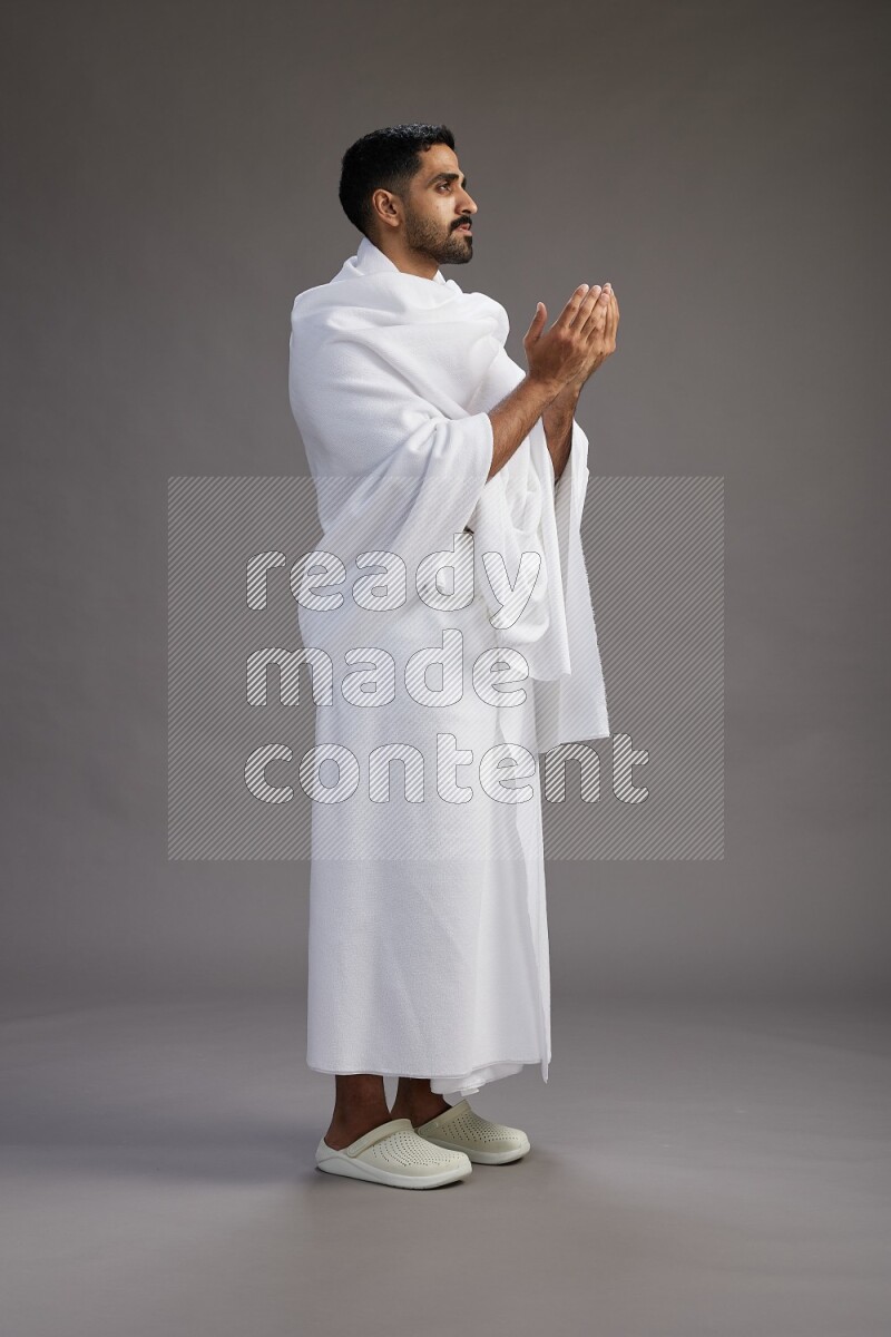 A man wearing Ehram Standing performing dua'a on gray background