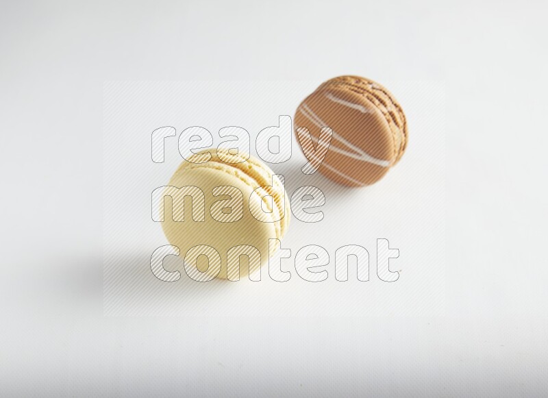 45º Shot of of two assorted Brown Irish Cream, and Yellow Vanilla macarons on white background