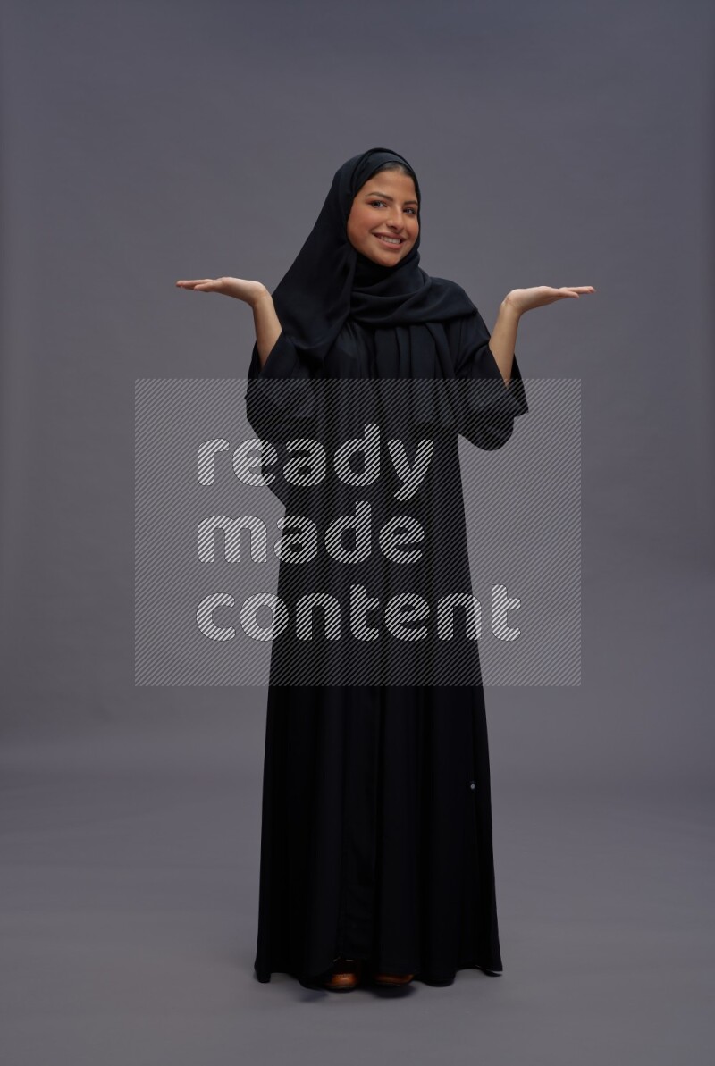 Saudi woman wearing Abaya standing interacting with the camera on gray background