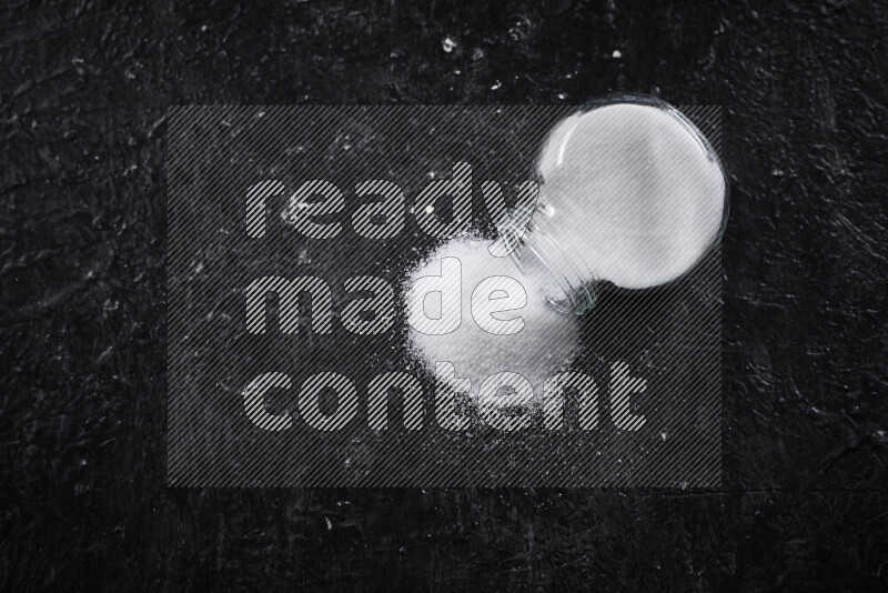 A glass jar full of fine table salt on black background