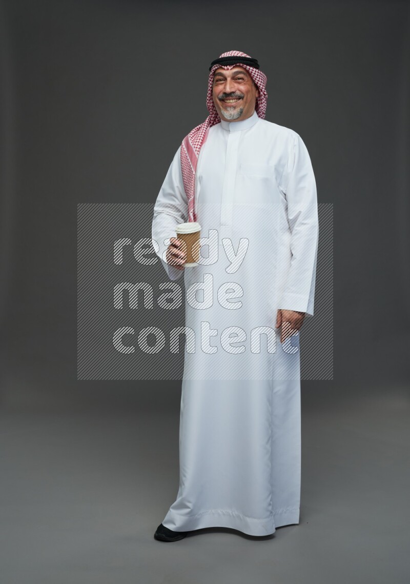Saudi man with shomag Standing holding paper cup on gray background