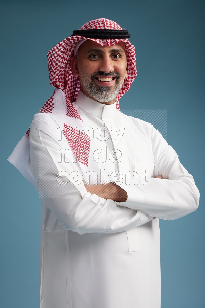 Saudi man wearing thob and shomagh posing to the camera on blue background