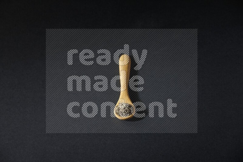 A wooden spoon full of cumin seeds on black flooring